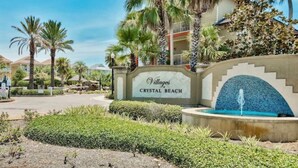 Une enseigne indiquant « Villages Crystal Beach », avec une fontaine et des palmiers en arrière-plan.