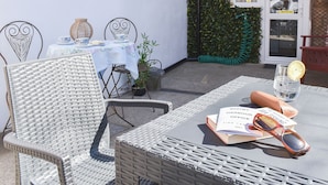 Un área de estar al aire libre con sillas de mimbre, una mesa, un libro y un vaso de agua.