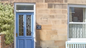 Una puerta azul con un panel de vidrio, una pared de piedra y una ventana con cortina.