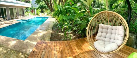 A wooden deck with a wicker chair and a pool.
