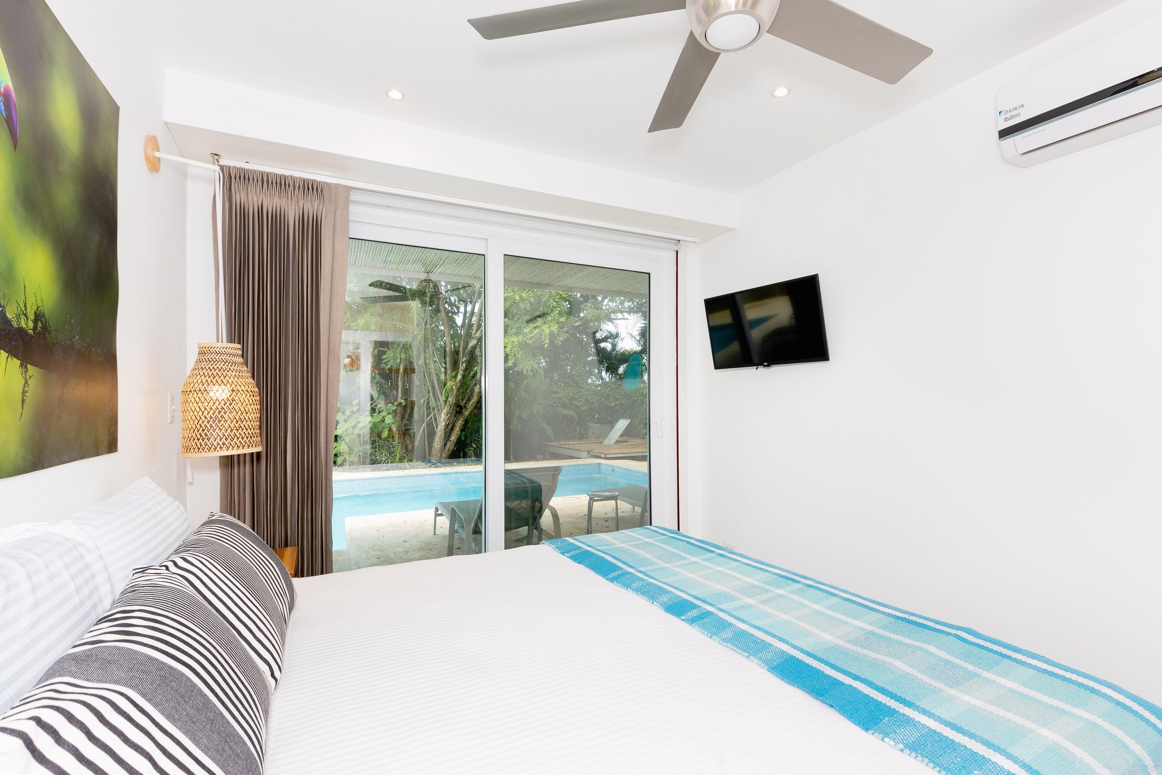 A bedroom with a bed, a TV, and a view of a swimming pool.