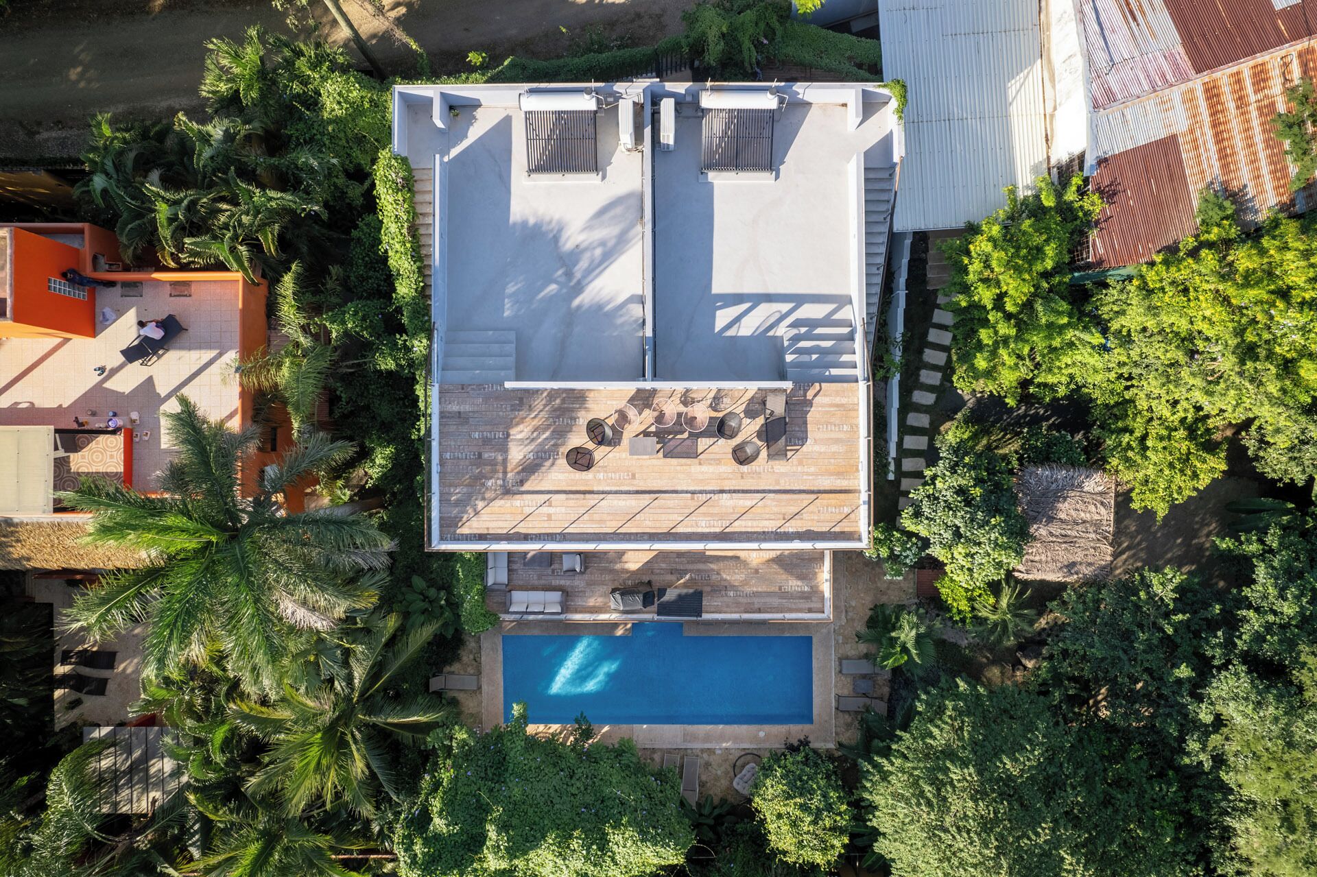 An aerial view of a residential property with a rooftop terrace, a swimming pool, and lush surrounding vegetation.