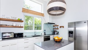 Eine moderne Küche mit weißen Schränken, einem Edelstahlkühlschrank, einem eingebauten Backofen und einem großen Fenster mit Blick auf Grünflächen.