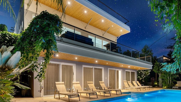 Ein modernes, zweistöckiges Haus mit Swimmingpool, Sitzgelegenheit im Freien und einem Balkon mit Blick auf den Pool.