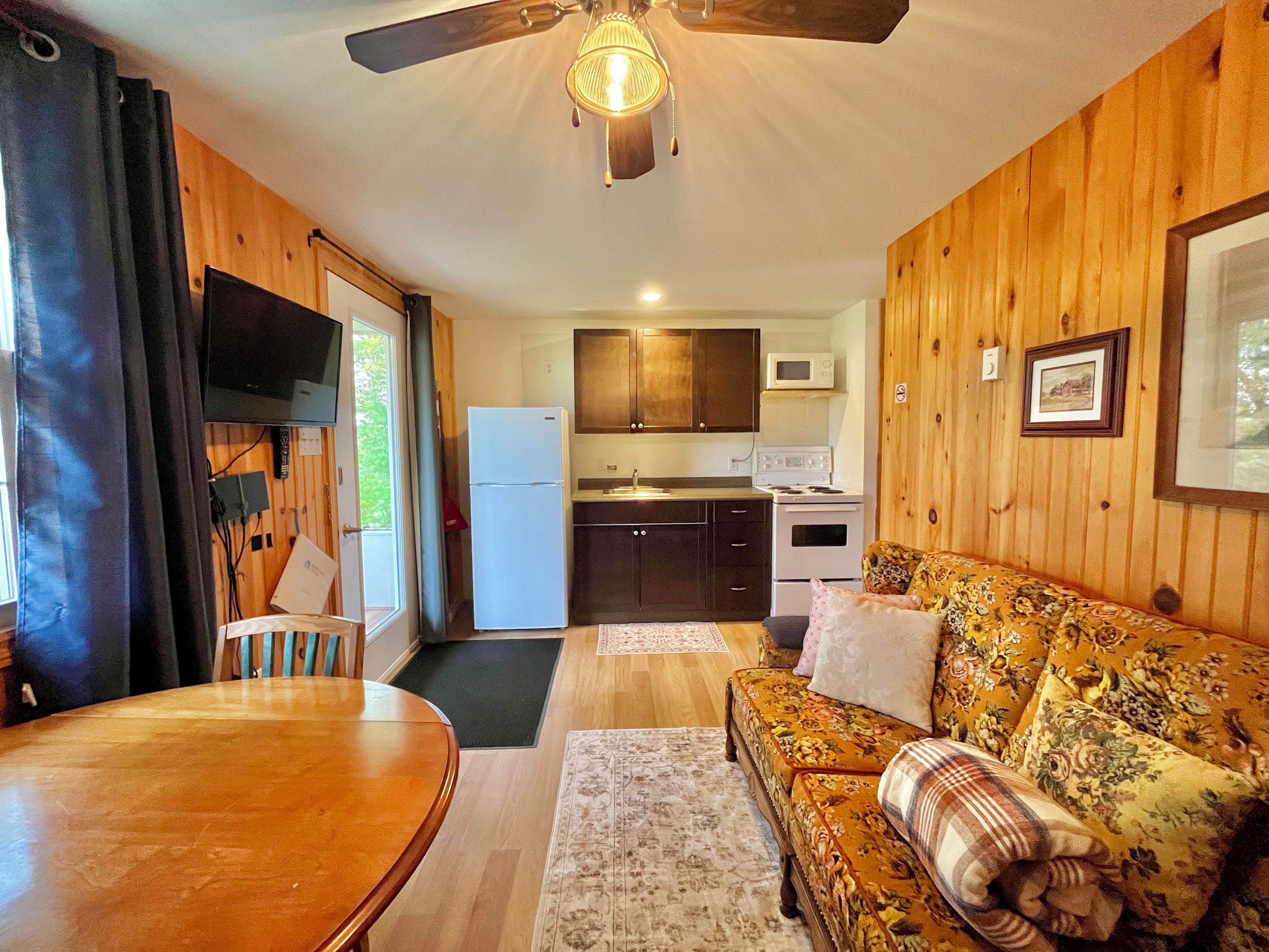 A compact living space with a dining area, sofa, kitchen, and a ceiling fan.