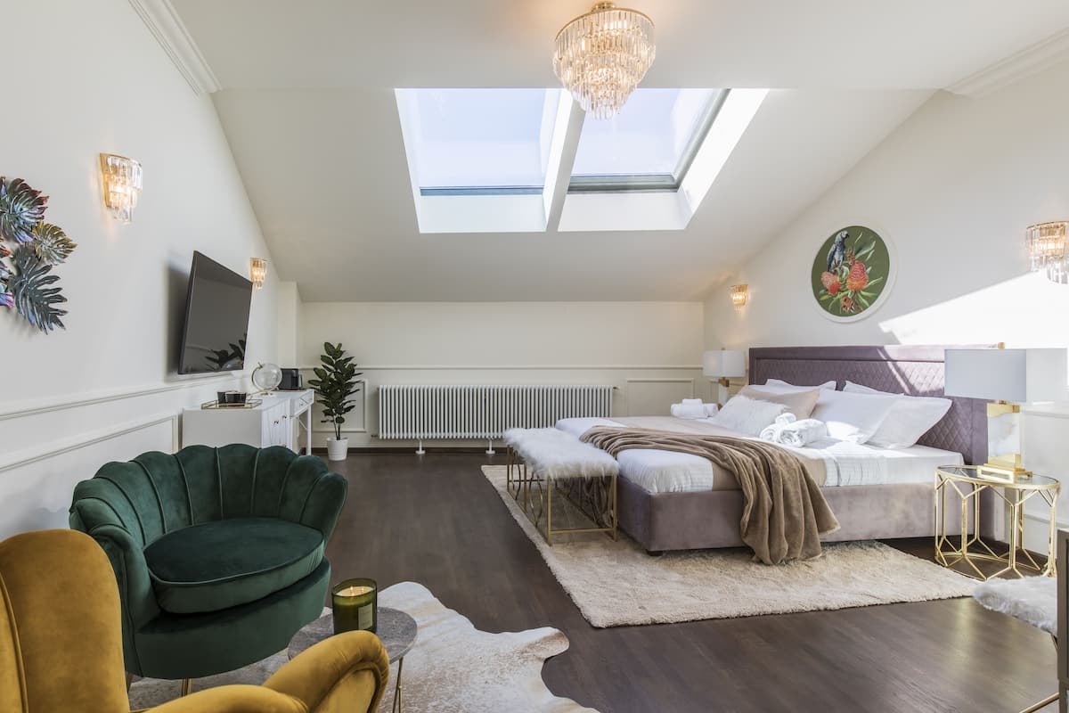 A modern bedroom with a skylight, a bed, a green armchair, and a small round table.