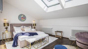 A modern bedroom with a skylight, a bed with a white and blue duvet, a round gold-framed bedside table, a purple armchair, and a white radiator.