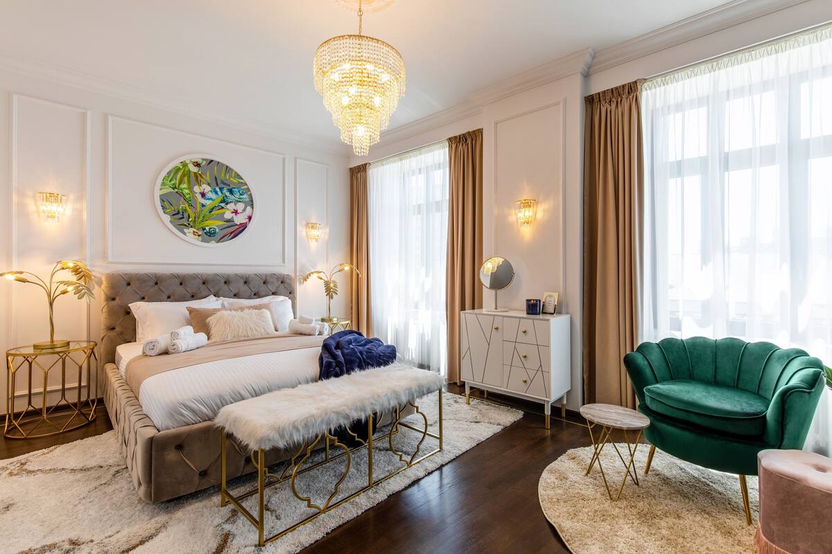 A bedroom with a large bed, a chandelier, a green armchair, and a round painting on the wall.