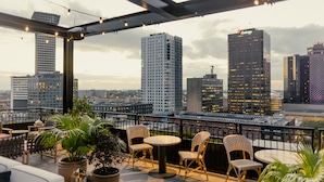 A rooftop terrace with outdoor seating, potted plants, and a city skyline view.