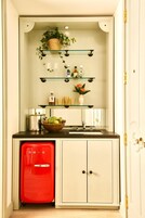 Cocina compacta con un refrigerador rojo, un lavamanos y una encimera con estantes que contienen diversos objetos.