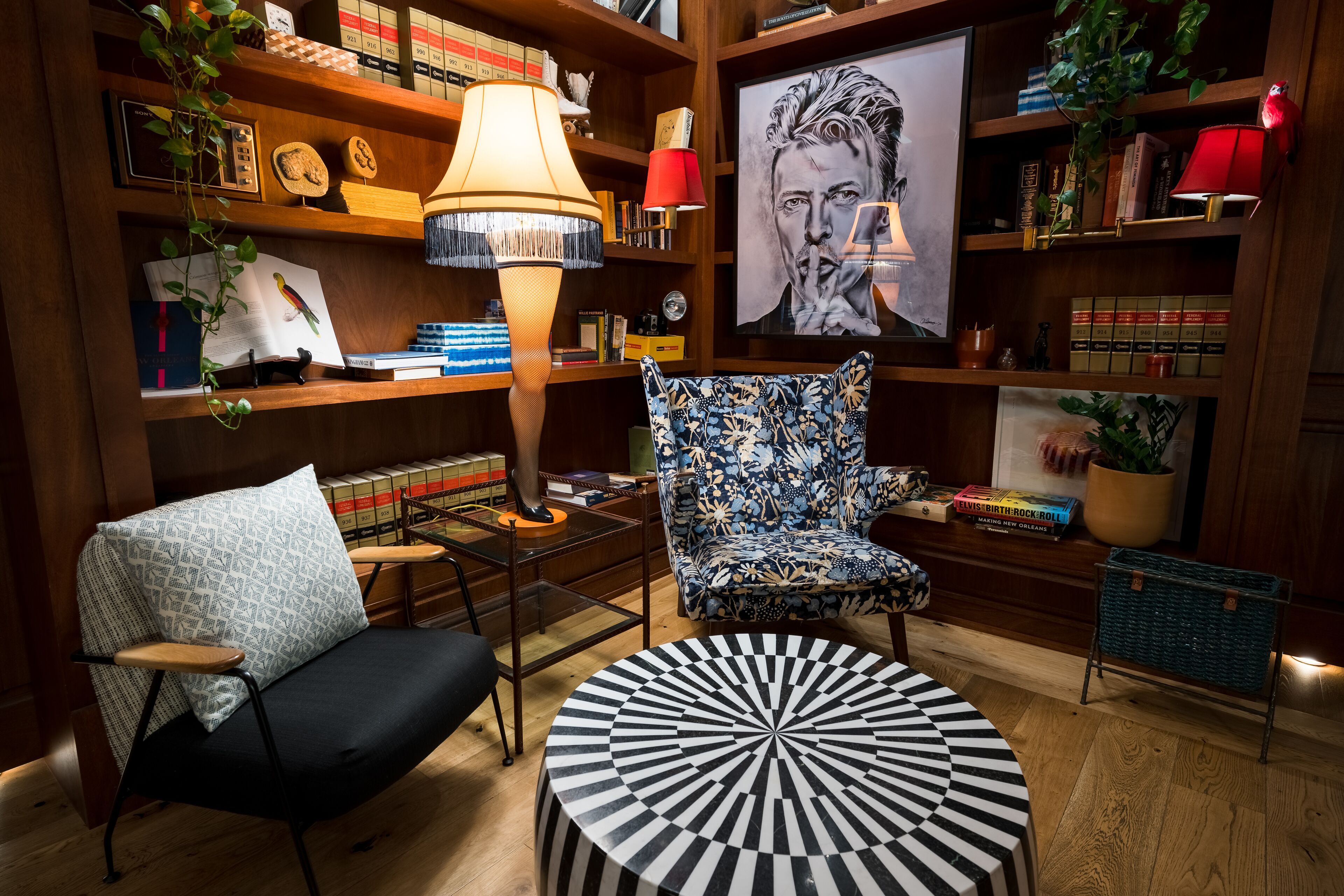 A cozy reading nook with a patterned armchair, a round black and white table, and a bookshelf filled with books and decorative items.
