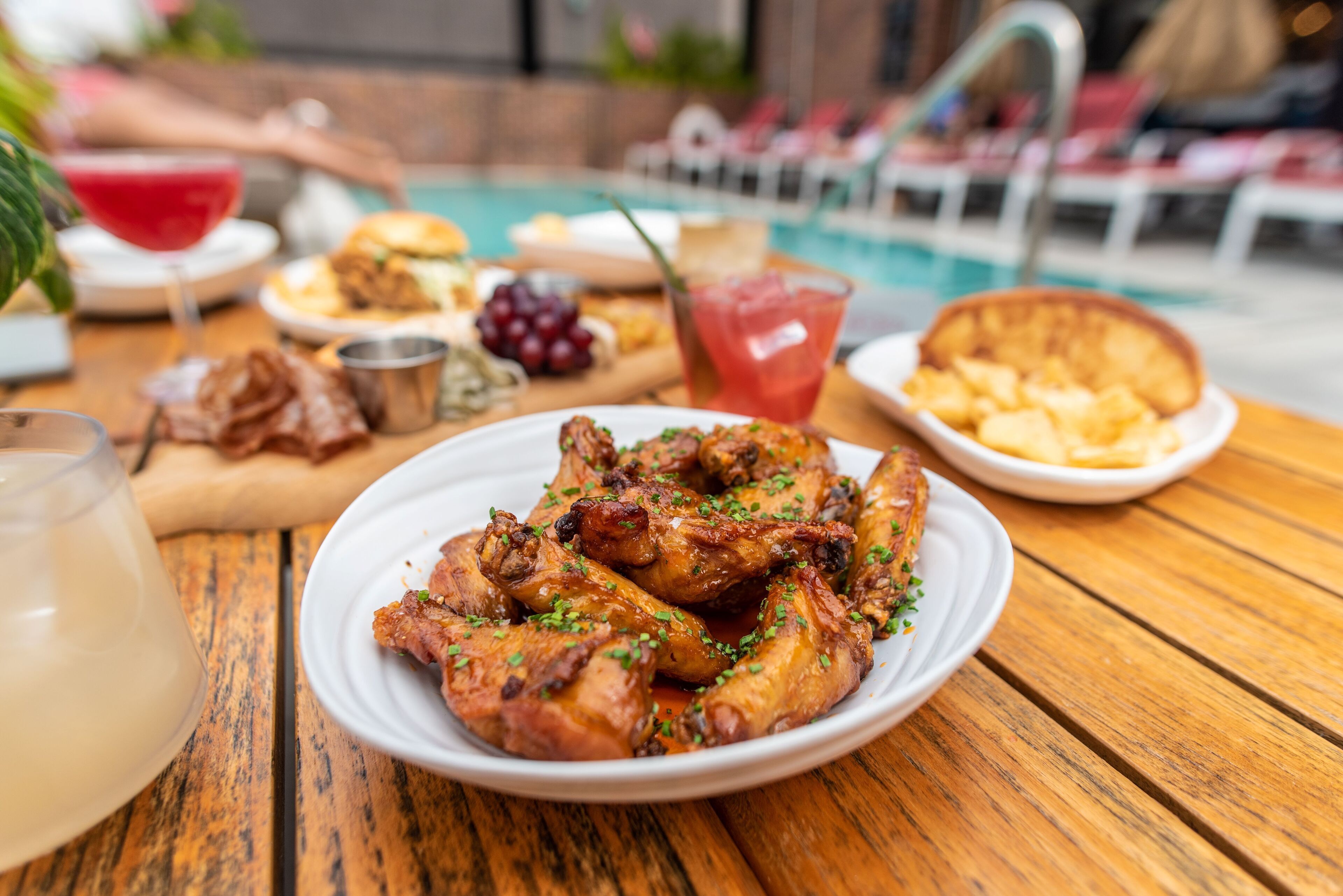 A wooden table with a plate of grilled chicken wings, a glass of red drink, and various side dishes.