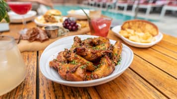 Una mesa de madera con un plato de alitas de pollo a la parrilla, un vaso de bebida roja y diferentes acompañamientos.