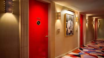 Un pasillo de hotel con una puerta roja, apliques de pared estampados y una alfombra colorida.