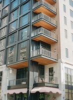Un edificio de varios pisos con balcones, ventanas amplias y terrazas con mesas y sillas.