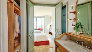 Quarto com guarda-roupa de madeira, cama com um tapete vermelho, banheiro com espelho, pia e uma planta.