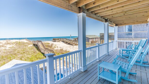 A wooden deck with blue Adirondack chairs overlooking a beach with a wooden walkway leading to the water. - 5848- Sun & Sea time - Oceanfront Escape | Pool, Hot Tub, Sleeps 18 (Nags Head)