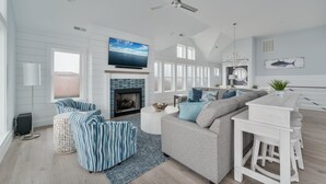 A spacious living room with a fireplace, a large TV, and a ceiling fan. - 5848- Sun & Sea time - Oceanfront Escape | Pool, Hot Tub, Sleeps 18 (Nags Head)