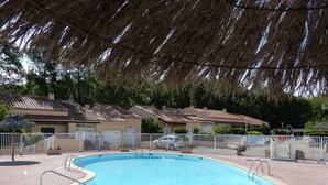 A swimming pool with a white fence, surrounded by houses with tiled roofs and a thatched roof overhead. - Familienurlaub, Haustiere, Sonne, Meer, Wandern, Radfahren (Argelès-sur-Mer)