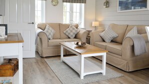 A cozy living room with two beige sofas, a wooden coffee table, and plaid curtains.