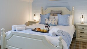 A neatly made bed with a tray of croissants and juice, two bedside tables with lanterns, and a painting of a beach scene on the wall.