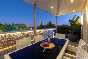 An outdoor seating area with a table, chairs, a bottle, and a bowl of fruit.