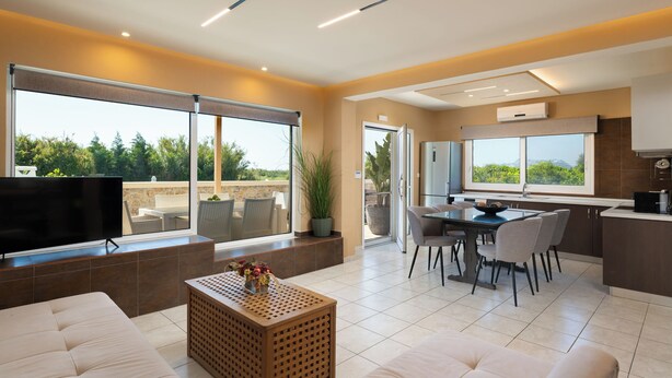 A modern living room with a sofa, a coffee table, and a TV. There is a dining area with a table and chairs.