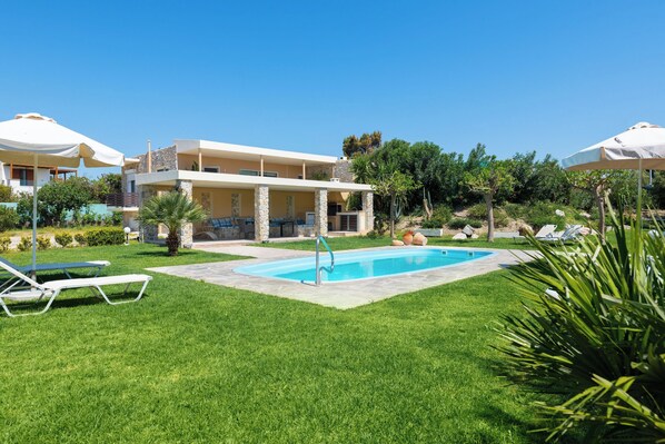 A pool with lounge chairs, a building with balconies, and surrounding greenery.