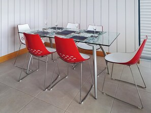 A glass-top dining table with four red chairs, a white wall, and a window with blinds.
