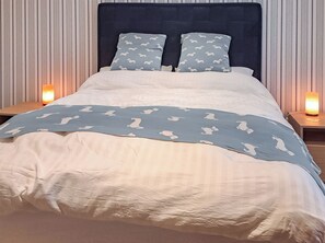 A bed with a dark headboard, two pillows with a light blue pattern, a matching blue throw blanket, and two bedside lamps.