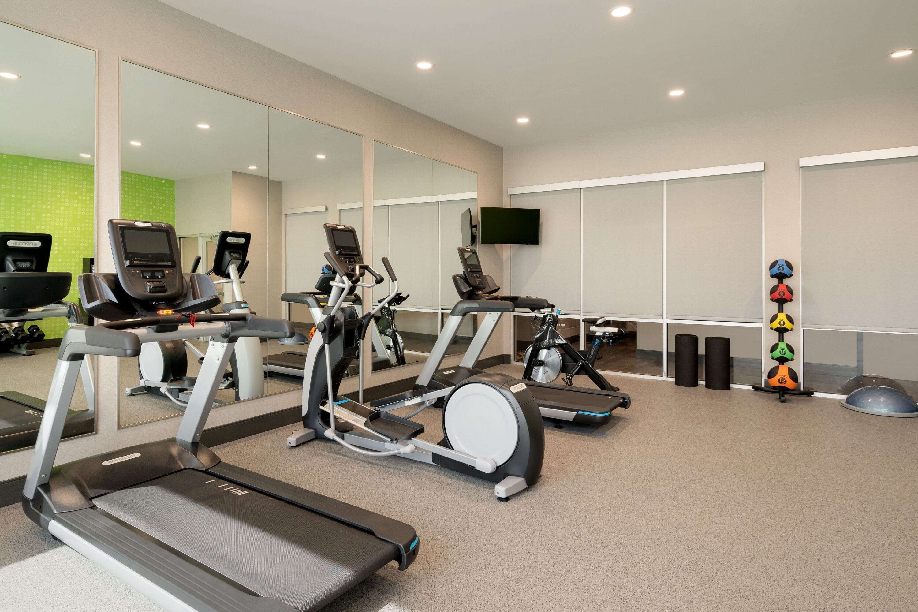 A gym with treadmills, stationary bikes, and a TV on the wall.