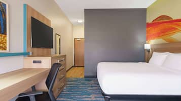 Quarto de hotel com cama, escrivaninha, cadeira, televisão e obras de arte nas paredes.
