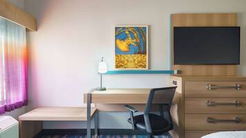 Une chambre d’hôtel comprenant un lit, un bureau avec une chaise, une télévision, un tableau et une commode.