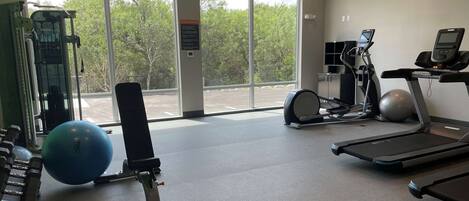 Un gimnasio con equipo de ejercicio, un ventanal y vistas a árboles.