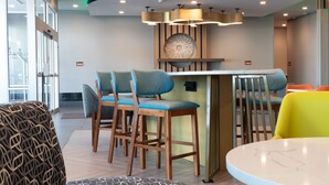 Eine moderne Bar mit Holzhockern und einem Marmortisch, umgeben von Sitzgelegenheiten mit gemusterten Kissen.
