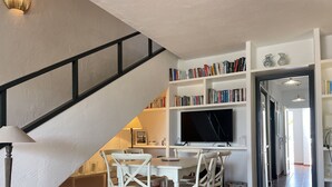 Ein Essbereich mit Tisch und Stühlen, einem an der Wand befestigten Fernseher und einer Treppe, die zu einer anderen Ebene führt.