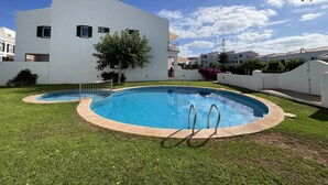 Ein Wohngebiet mit einem Schwimmbad, umgeben von einer grünen Rasenfläche, einem weißen Gebäude mit zahlreichen Fenstern und blauem Himmel.