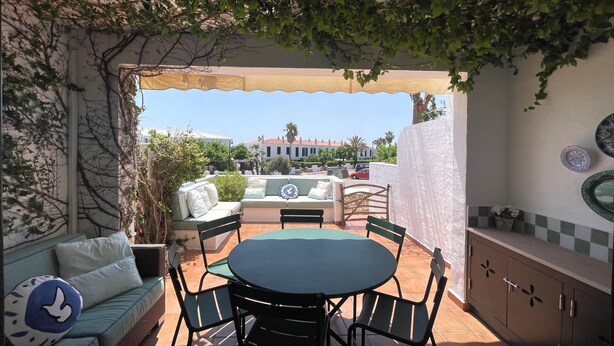 Eine Terrasse im Freien mit einem runden Tisch und Stühlen, einer Couch und einer Pergola mit Kletterpflanzen.