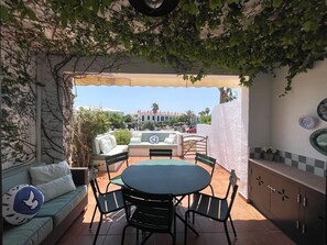 Eine Terrasse im Freien mit einem runden Tisch und Stühlen, einer Couch und einer Pergola mit Kletterpflanzen.