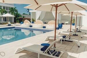 Un área junto a la piscina con sillones de descanso, sombrillas y una alberca.