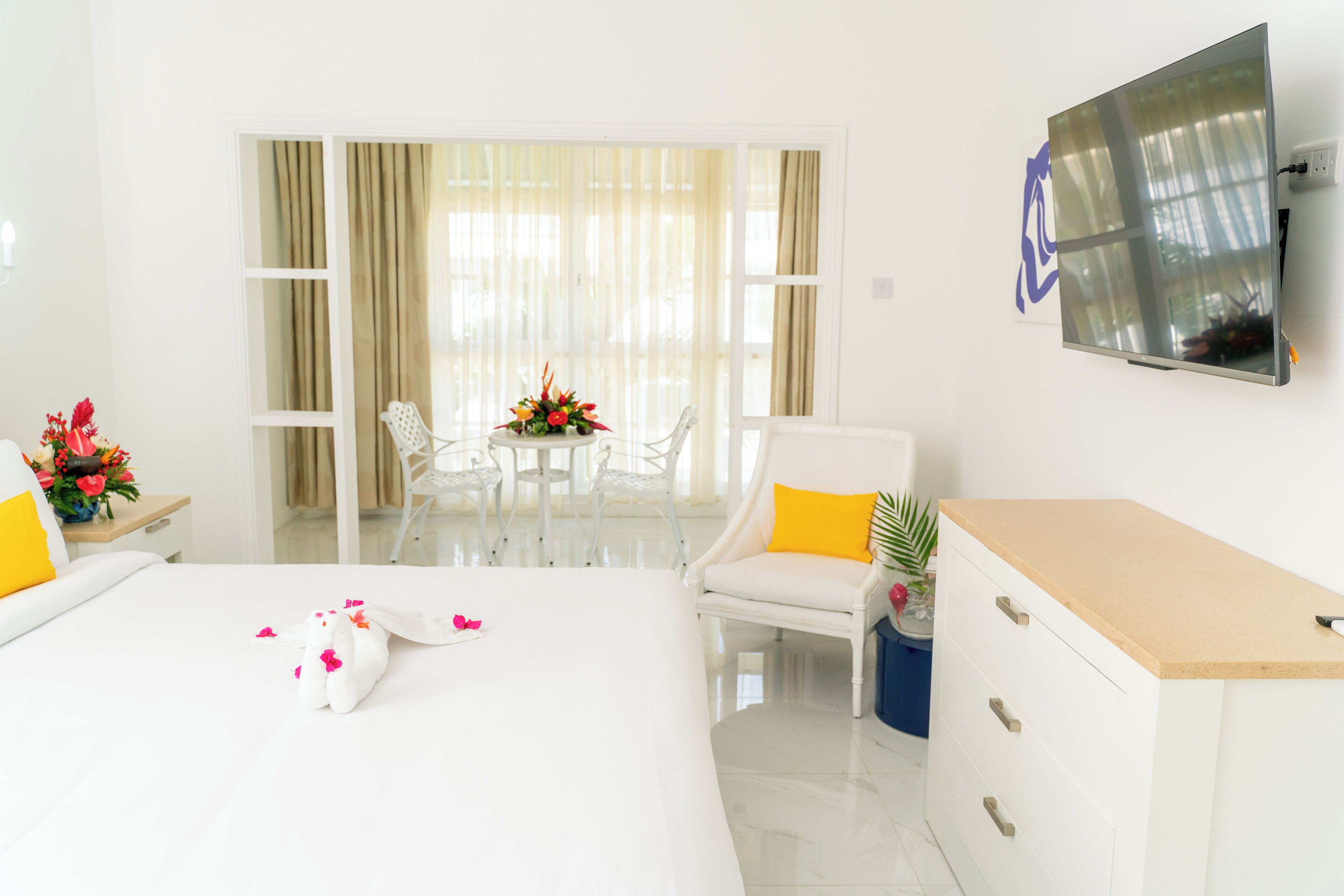 A hotel room with a bed, a desk, a chair, a TV, and a balcony with curtains.