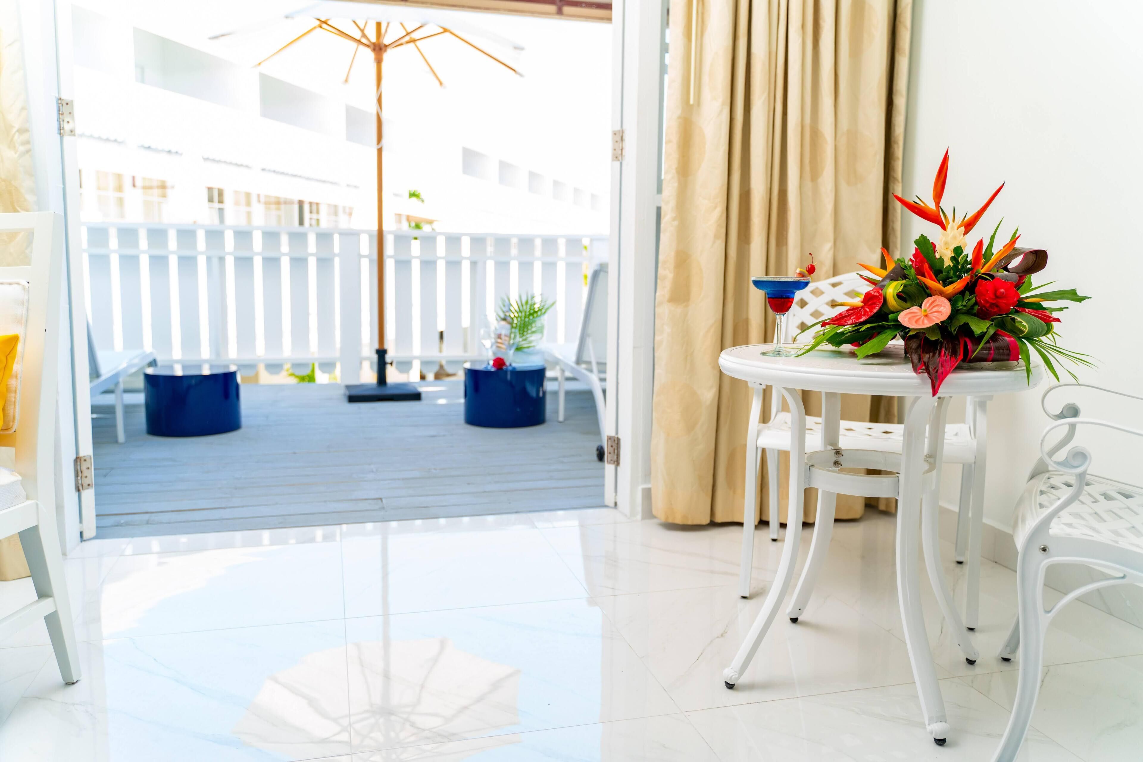 A room with a view of a wooden deck, a white table with a flower arrangement, and a white chair.