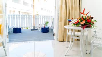 Una habitación con vistas a una terraza de madera, una mesa blanca con un arreglo floral y una silla blanca.