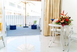 Una habitación con vistas a una terraza de madera, una mesa blanca con un arreglo floral y una silla blanca.