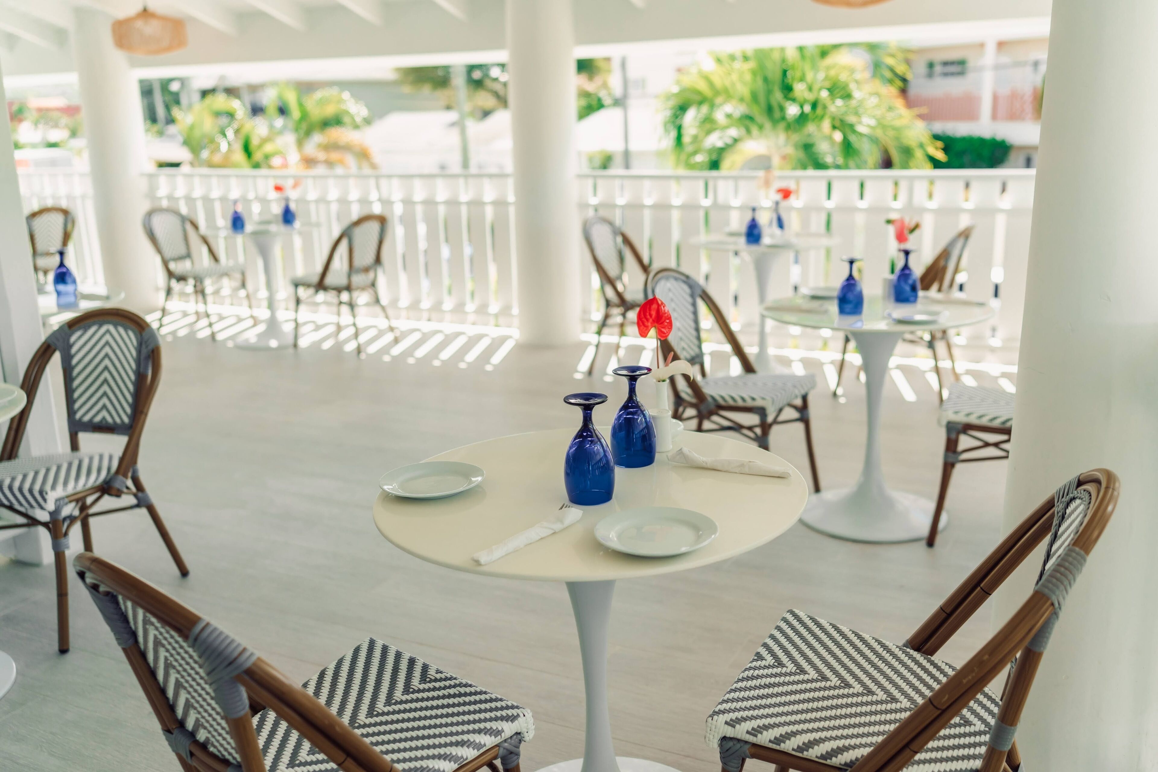 Un restaurant avec des tables rondes et des chaises en osier, agrémenté de vases bleus et d’assiettes blanches.