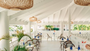 A covered outdoor seating area with wicker ceiling lamps, white railings, and tables with blue vases.