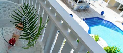 A balcony with a clear view of a swimming pool, a bar area, and a dining setup.