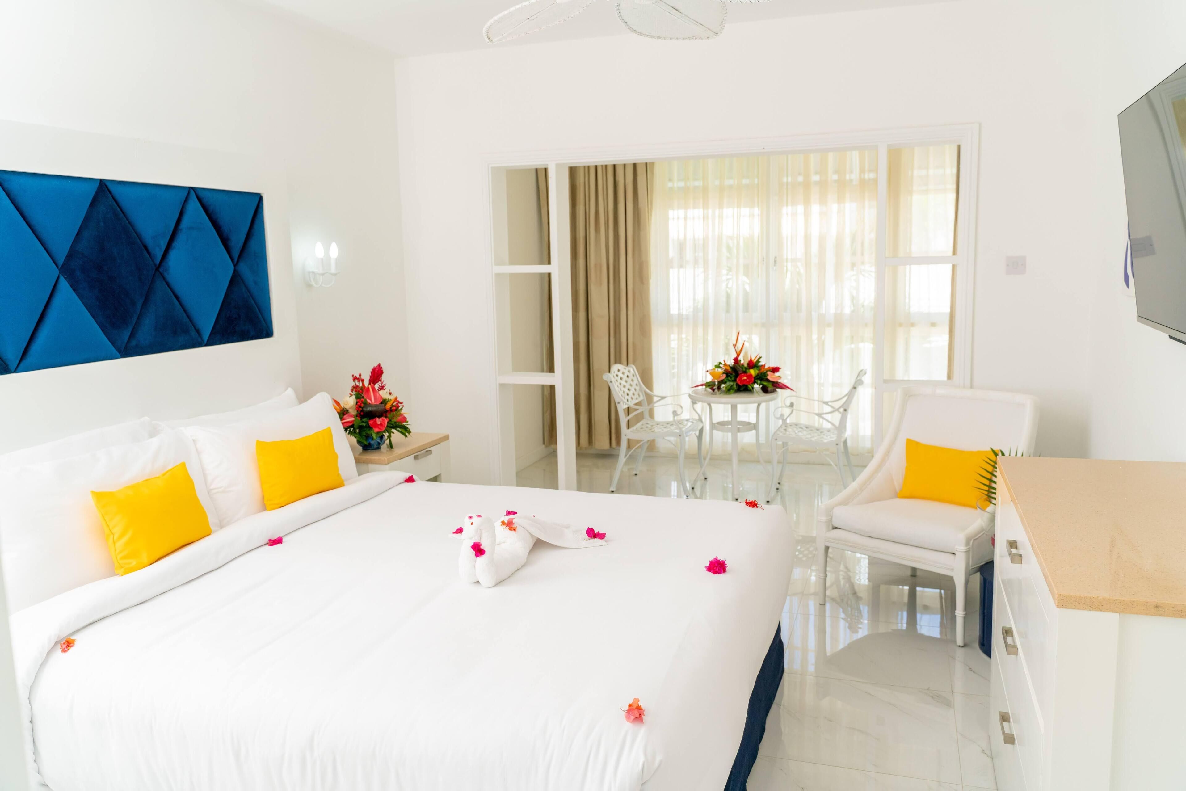 A hotel room with a large bed, a desk, a chair, and a balcony with a table and chairs.