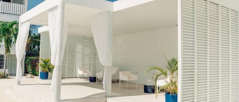 A modern outdoor lounge area with white furniture, covered by white canopies, and potted plants.