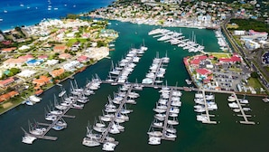 An aerial view of a marina with numerous boats docked, surrounded by residential buildings and a hilly landscape in the background.